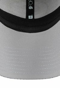Base d'une casquette New Era 9FORTY grise et noire montrant des coutures détaillées et l'étiquette de la marque à l'intérieur du chapeau.