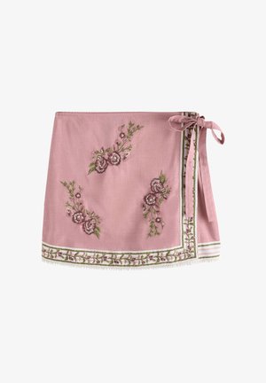 Jupe portefeuille rose avec broderie florale, ourlet bordé de vert et blanc et un nœud noué sur le côté.