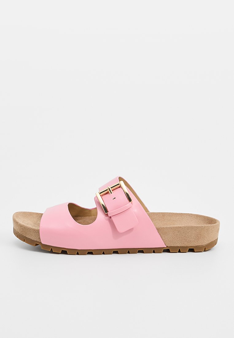 Sandale rose à glissière avec une finition brillante, conception ouverte à l'avant et un détail de boucle dorée. Semelle intérieure en beige texturé et semelle en caoutchouc.