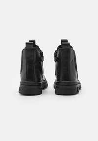 Botas de tobillo de cuero negro con un acabado texturizado, que presentan una puntera redondeada, paneles laterales elásticos y una suela de goma plana.