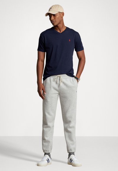 Marinblå v-ringad t-shirt, grå sweatpants med elastiska mudd, och vita sneakers med marinblå ränder, toppat med en beige keps.