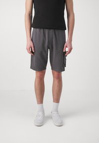 Shorts en coton gris avec une coupe décontractée, dotés de poches latérales et d'une taille à cordon. Portés avec un débardeur noir et des baskets blanches.