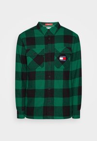Camicia in flanella a quadri verde e nera con design a bottoni, due tasche sul petto e una piccola etichetta con marchio sulla tasca sinistra.