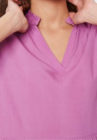 V-ringad blus i lavendeltyg med volangkrage och mjuk textur, med en fin söm längs fållen.