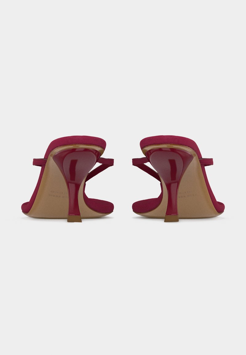 Paire de mules rouges à talons aiguilles fins et bouts ouverts, vues de dos sur fond blanc.