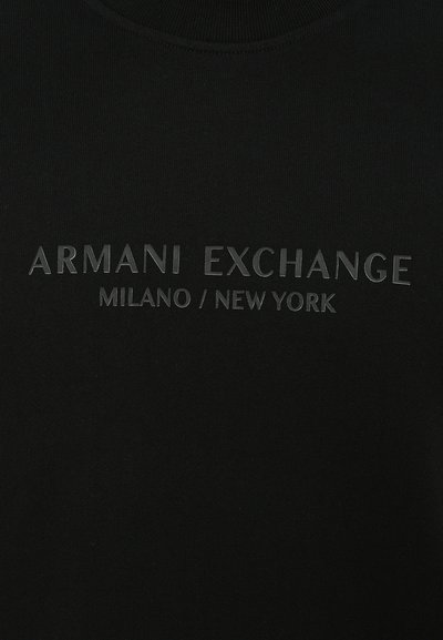T-shirt en coton noir avec texte en relief "ARMANI EXCHANGE MILANO / NEW YORK" dans une teinte contrastante, avec une texture lisse et un col rond.