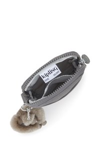 Kleine graue Kipling-Tasche mit geöffnetem Reißverschluss, die das Innenetikett und die textile Fütterung zeigt, befestigt an einem flauschigen Schlüsselanhänger-Zubehör.