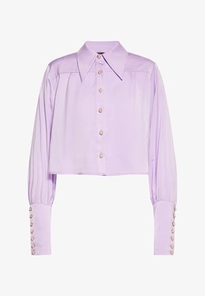 Levendula színű, rövidített ing, strukturált gallérral, gyöngy gombokkal és plissé hosszú ujjakra. Simább, fényes anyagból készült.