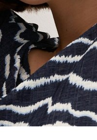 Navy fabric with white zigzag pattern, featuring a textured surface and a draped design. The neckline has soft, ruffled details.