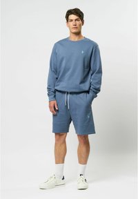Blauwe sweatshirt en bijpassende shorts van zachte stof, met een geborduurd logo, witte trekkoorden en witte sport sneakers.