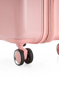 Maleta rígida rosa con una superficie texturizada, que cuenta con cuatro ruedas negras y una base rosa a juego. Compartimentos con cremallera visibles.