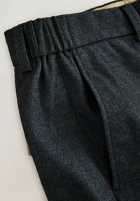 Dark woven trousers featuring a textured fabric, elastic waistband, and side pockets. The design emphasizes simplicity and utility.