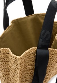 Borsa tote in paglia intrecciata con bordo superiore a onde, manici in tessuto nero e interno liscio verde oliva.