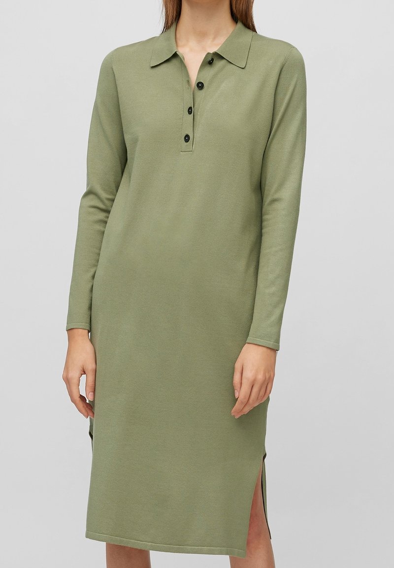 Robe à manches longues, longueur genou, en vert olive avec un col, patte de boutonnage, fentes latérales et un tissu doux et texturé.