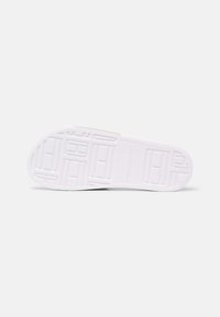 Semelle de chaussure blanche avec des motifs géométriques et le nom de la marque "Tommy Hilfiger" embossé au centre sur un fond blanc uni.