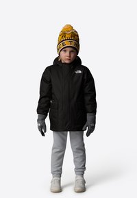 Black insulated jacket with a hood, gray gloves, light gray sweatpants, and a yellow patterned beanie with “FACE THE” text on a child.