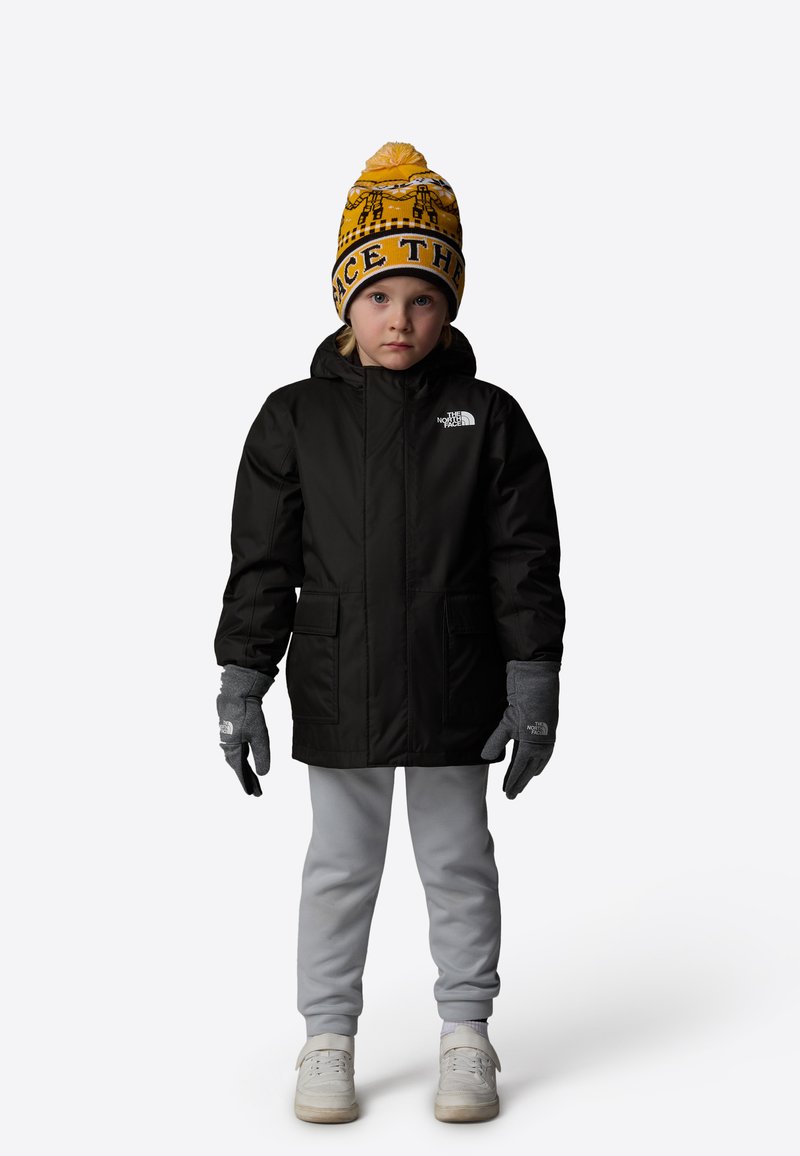 Black insulated jacket with a hood, gray gloves, light gray sweatpants, and a yellow patterned beanie with “FACE THE” text on a child.
