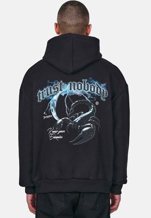 Sort oversized hættebluse med et grafisk print, der har teksten "trust nobody", en skorpion og lyn-accenter på ryggen.