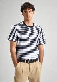 Juostuota marškinėliai baltos ir tamsiai mėlynos spalvos. Trumpomis rankovėmis, apvaliu kaklu, pagaminti iš minkštos medvilnės. Suderinti su smėlio spalvos kelnėmis ir juodu diržu.