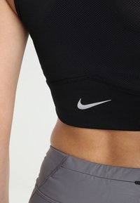 Gros plan sur la taille d’une personne portant un soutien-gorge de sport Nike noir avec logo et un legging de sport gris.