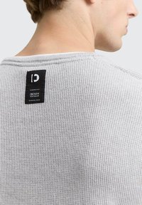 Grauer gerippter Pullover aus strukturiertem Stoff. Verfügt über ein schwarzes Markenetikett am hinteren Kragen mit weißem Text. Lässiges Design.