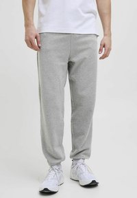 Grå sweatpants lavet af blødt stof, med elastisk talje og manchetter, sidelommer og en afslappet pasform. Bæres med hvide sneakers.
