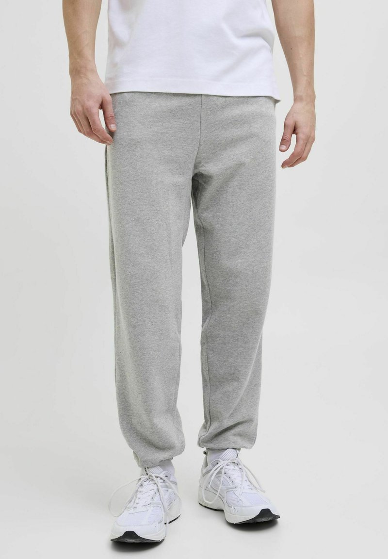 Grå sweatpants lavet af blødt stof, med elastisk talje og manchetter, sidelommer og en afslappet pasform. Bæres med hvide sneakers.