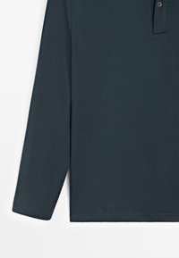 Granatowa, długorękawowa koszulka polo wykonana z miękkiej tkaniny, z dwoma guzikami przy dekolcie oraz subtelnym przeszyciem wzdłuż brzegu i mankietów.