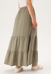 Jupe maxi tiered olive, en tissu léger avec une taille élastique ; assortie à des baskets crème.
