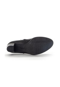 Chaussure en cuir noire avec un faible talon, semelle texturée et une marque visible. Dessus lisse avec un design simple et courbé et un minimum de détails.
