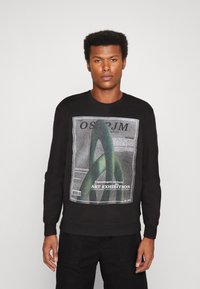 Czarny sweatshirt z graficznym nadrukiem przedstawiającym zielone krzywe i tekst. Ściągacze przy mankietach i u dołu, wykonany z materiału bawełnianego z domieszką. Prosty i casualowy design.