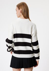 Wzorzysty sweter w biało-czarną kratę o luźnym kroju, z opadającymi ramionami i ściągaczami na mankietach, zestawiony z plisowaną czarną spódnicą.