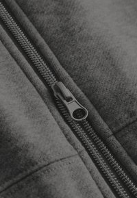 Zwarte stoffen kleding met rits, gekenmerkt door een gladde textuur, zichtbare stiksels en een duurzame metalen rits. Close-up van het ritsdetail.