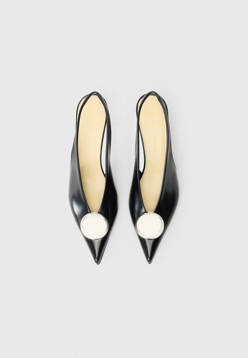 Tacones slingback de cuero negro con punta afilada, que cuentan con un acento circular blanco en la parte superior y un interior beige. Textura suave.