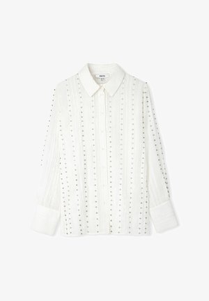 Chemise blanche à manches longues avec un col boutonné, ornée de rangées verticales de petits clous en argent et d'un tissu texturé.
