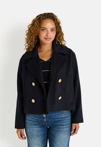 Manteau peacoat court bleu marine en tissu doux avec un design à double boutonnage, de grands boutons dorés et un col cranté. Comprend des poches latérales et une coupe droite.