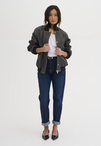 Gray bomber jacket with a smooth texture, ribbed black cuffs, zipper closure, paired with rolled cuff dark blue jeans and black heels.
