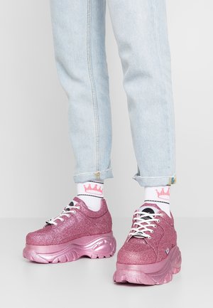 Person wearing light blue rolled-up jeans, white socks with pink crown patterns, and glittery pink platform sneakers with white laces.