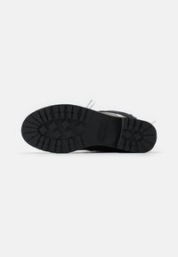 Black rubber shoe sole with a textured tread pattern, featuring branding "KARL" and a round toe design. Smooth surrounding areas.
