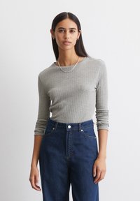 Grijze geribbelde langledemige top met een ronde halslijn. Gecombineerd met donkerblauwe high-waisted spijkerbroek. Eenvoudige zilveren ketting.