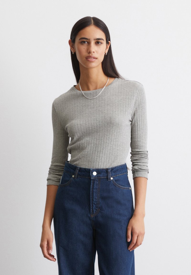 Grijze geribbelde langledemige top met een ronde halslijn. Gecombineerd met donkerblauwe high-waisted spijkerbroek. Eenvoudige zilveren ketting.