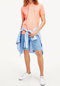 Kortärmad, ljus korallfärgad pikétröja matchad med ljusblå denimshorts. Vita sneakers. Ljusblå skjorta knuten runt midjan.