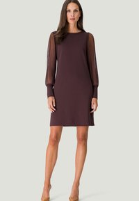 Brun skiftedresse med lange, gennemsigtige organzaærmer, rund halsudskæring og tætsiddende silhuet. Glat stof med en elegant finish.