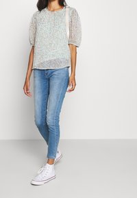 Jasnoniebieska bluzka w kwiaty z bufkami, zestawiona z jasnoniebieskimi skinny jeansami i białymi trampkami za kostkę. Gładki, przewiewny materiał.