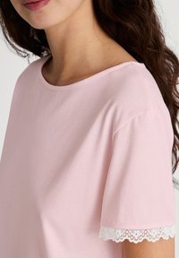 Lichtroze katoenen t-shirt met een ronde hals en korte mouwen, voorzien van een witte kanten rand langs de mouwranden. Zacht van textuur.