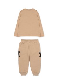 Maglia beige a maniche lunghe in cotone con bottoni a pressione sulle spalle e pantaloni della tuta beige abbinati con dettagli in testo nero sul lato.