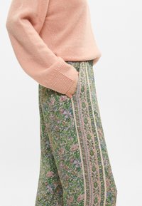 Φλοράλ σχέδιο, πράσινα παντελόνια με φαρδιά πόδια και ροζ και κρεμ κάθετες ρίγες, με μια πλευρική τσέπη, συνδυασμένα με μια υφασμάτινη ροζ ζακέτα.