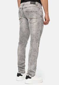 Jeans ajustados gris deslavado con un acabado texturizado, que cuentan con bolsillos traseros y una cinturilla de marca, combinados con zapatillas blancas.