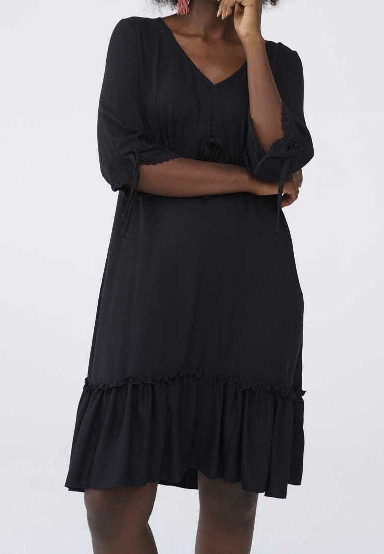 Svart klänning i mjukt tyg med V-ringning och trekvartslånga ärmar. Har samlade detaljer och en volangkant.