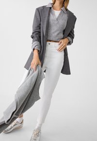 Gray plaid oversized blazer, gray cropped sweater, white high-waisted jeans, holding gray knit sweater, silver sneakers with reflective accents.
